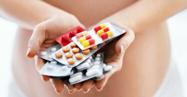schwangere Frau hält verschiedene Medikamente und Arzneimittel in der Hand
